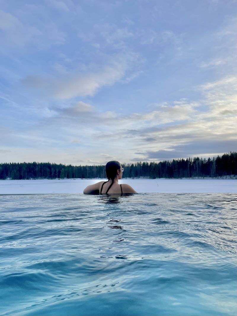 Marta numa piscina aquecida com vista para um lago gelado e floresta na Finlândia